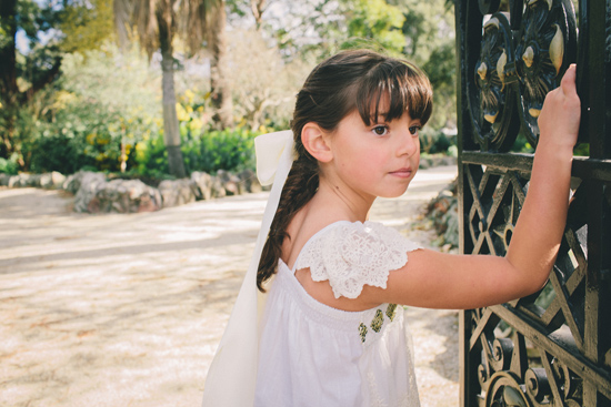 Flower girl in white dress with lace sleeves at iron gate